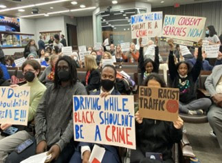 Masked protesters hold signs reading "Driving while Black shouldn't be a crime" and "End racist traffic stops."